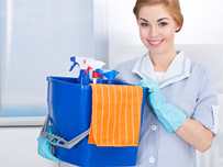 A lady in cleaning clothes and gloves holding a blue bucket full of cleaning supplies, spray bottles and cloths.